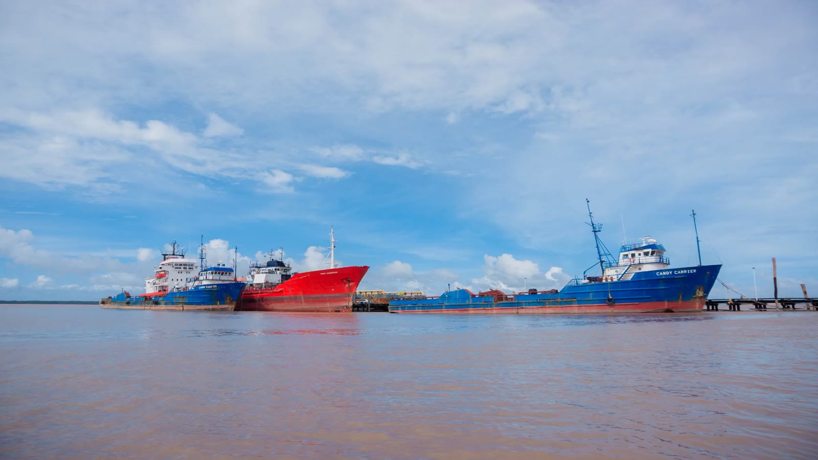 Three GCITI vessels lying alongside the wharf at Parika on the Essequibo river in Guyana, seen from the water.