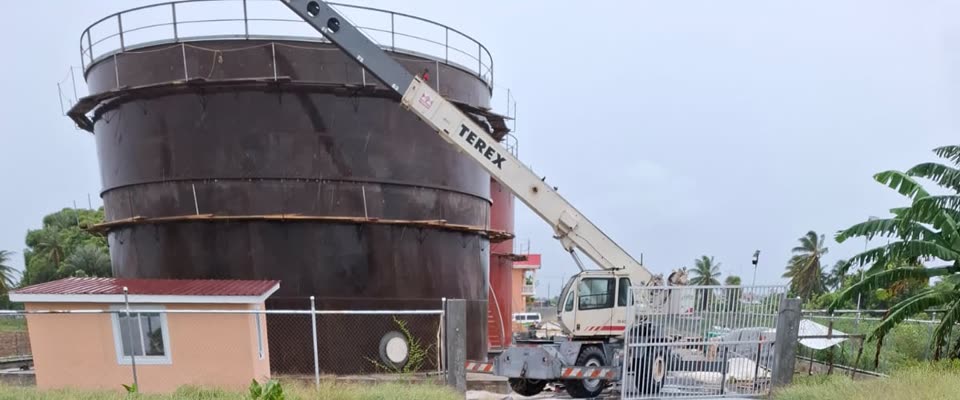 A bulk storage tank under erection and a mobile crane at GCITI’s Essequibo Coast site, behind the perimeter fence.