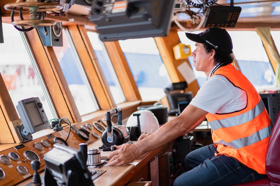 A GCITI officer at the wheelhouse console with a hand on the engine controls, radar and instruments in view.