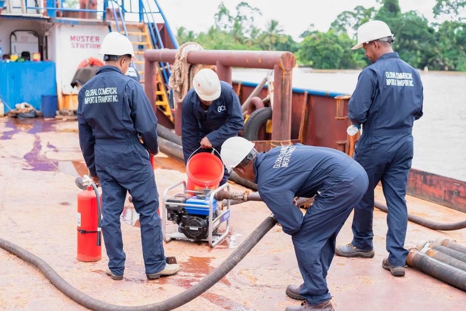 GCITI crew connecting a cargo hose to a portable transfer pump on a vessel deck, with a fire extinguisher stationed at the operation.